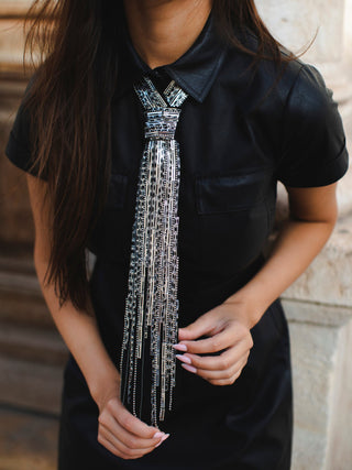 Person wearing a black shirt with an embroidered and beaded  decorative silver tie against a blurred background