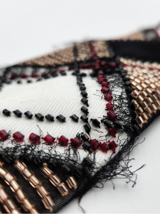 Close-up of an embroidered fabric with black, red, and gold glass beading, and black silk on a white background