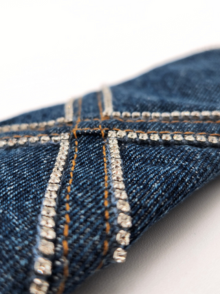 Close-up of blue denim fabric with rhinestone embellishments and gold top stitching