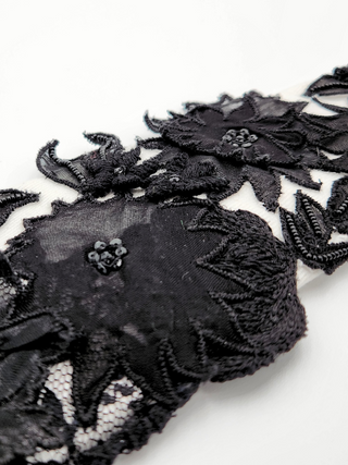 Close-up of black lace silk with floral embroidery and glass beads on a white cotton background
