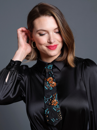 Model wearing a coral, turquoise and black embroidered petite necktie over a black silk shirt dress