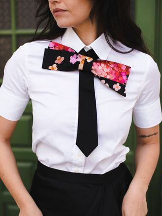 Model wearing a floral printed bow tie over a white blouse in front of a green door.