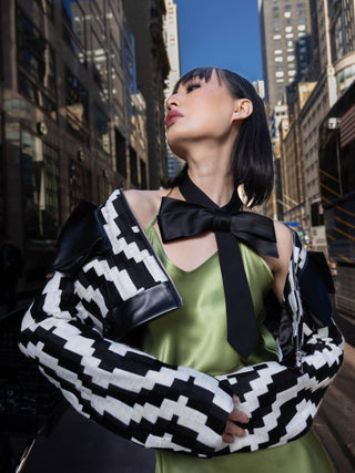 Model featuring a black bow tie styled with a green slip dress and geometric jacket on the streets of NYC.