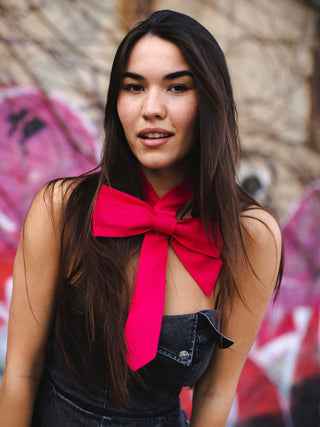 Model wearing a hot pink bow tie against a graffiti-covered wall.