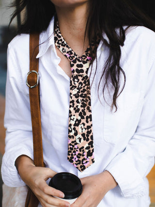 Model wearing a white shirt with a leopard print petite necktie holding a coffee.