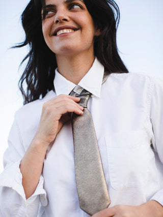 Model adjusting metallic leather petite tie worn over a white blouse.