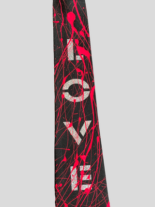 Closeup of black classic necktie with the word Love painted in silver and red splatter paint