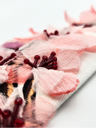 Closeup of pink silk petal embroidery and red glass beading on white cotton twill tie.