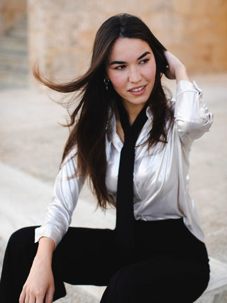 Model with long hair wearing a classic back necktie over a blouse with black pants.