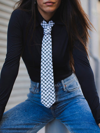 Model wearing a black shirt and blue jeans with a black and white houndstooth tweed tie.