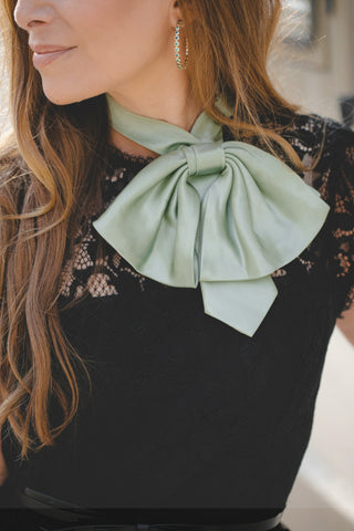 Woman wearing a black top with a sage green silk bow tie