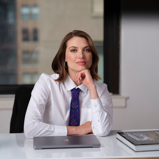 Female model sitting at her office desk in a crisp white blouse and purple embroidered tie with her laptop