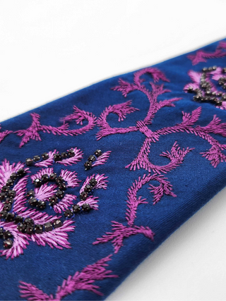 Closeup of purple baroque embroidery and crystal beading on royal blue necktie
