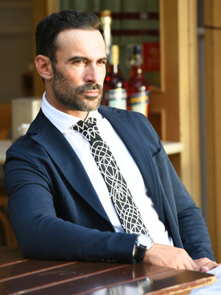Male model wearing a black necktie with white pearl embroidery with a navy suit and white shirt