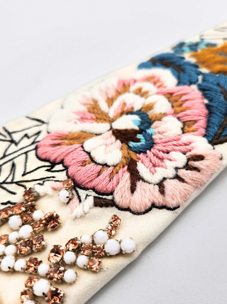 Closeup of embroidery in pinks and blue and crystal beading on ivory necktie