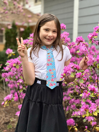 Young girl with a blue floral petite tie standing in front of pink flowers