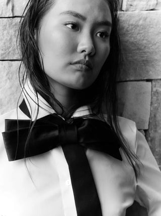 Black and white photo of a model wearing a large black bow tie against a stone background