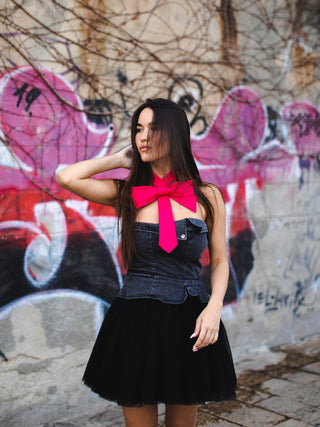 Model wearing a hot pink bow tie with a strapless denim top and black skirt in front of a graffiti-covered wall.