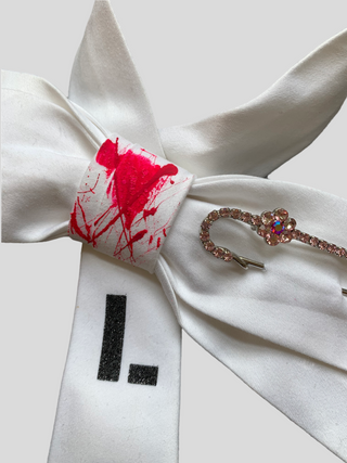 Detail of White bowtie with the word Love painted in black, red splatter paint on knot and crystal kilt pin