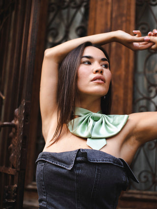 Model posing in strapless denim dress and sage green silk bow tie in front of wrought iron door
