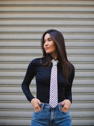 Model wearing a black long-sleeve top, blue jeans, and a houndstooth patterned tie against a metallic shutter background.